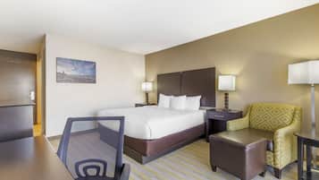 A hotel room with a bed, a desk, a chair, a small table, and a nightstand.
