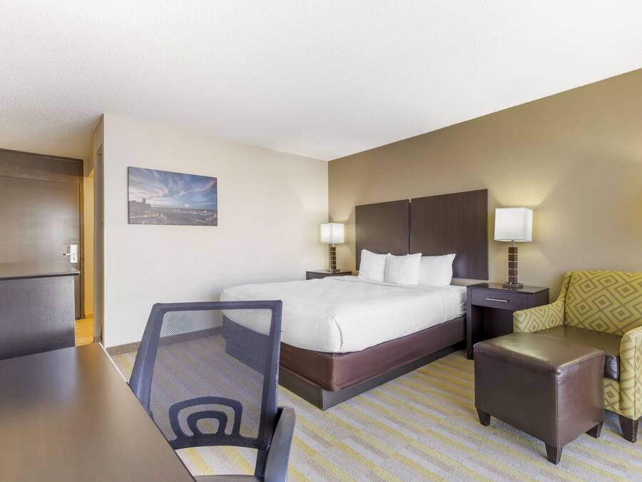 A hotel room with a bed, a desk, a chair, a small table, and a nightstand.