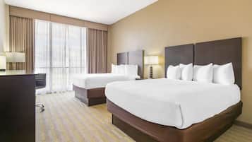 A hotel room with two beds, a desk, and a large window with curtains.