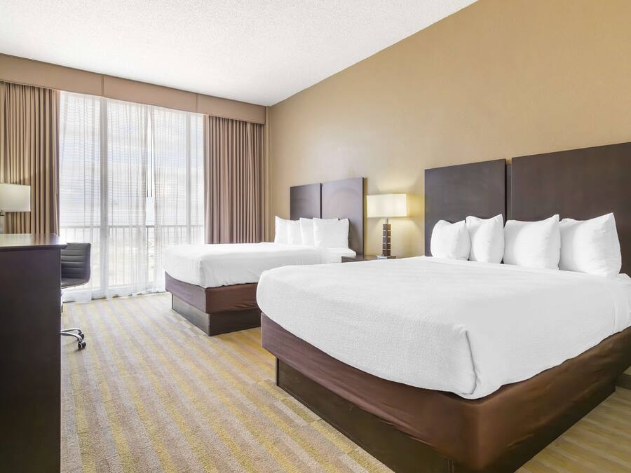 A hotel room with two beds, a desk, and a large window with curtains.