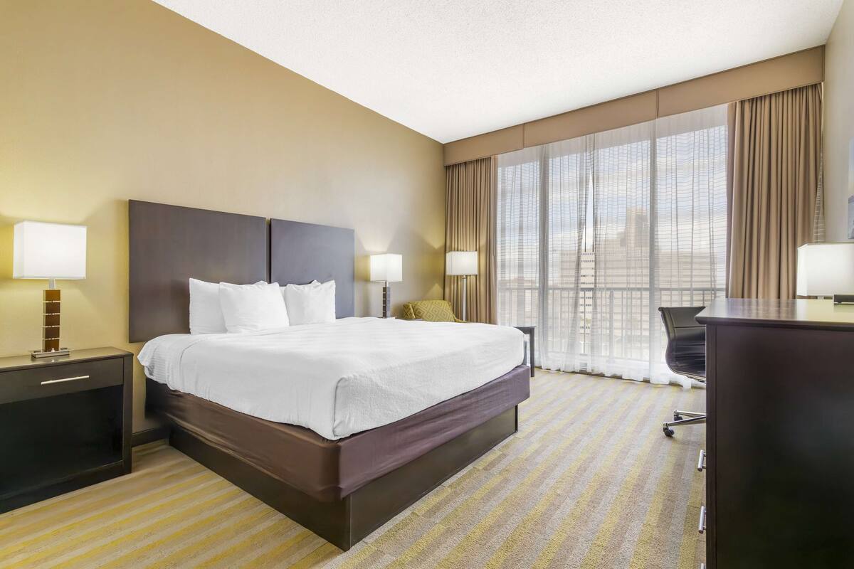 A hotel room with a large bed, two bedside tables with lamps, a desk, and a chair.