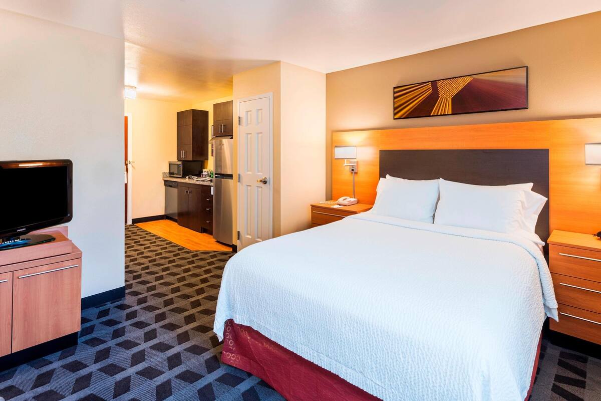 Een hotelkamer met een groot bed, een televisie op een houten kast, een magnetron en een koelkast in de kitchenette.