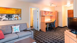 Una habitación de hotel compacta con sofá, un escritorio pequeño, televisión y alfombra estampada.