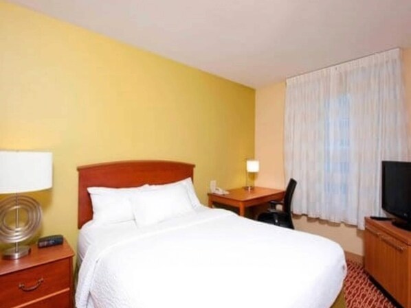 Habitación de hotel con cama, escritorio, silla, televisor y lámpara.