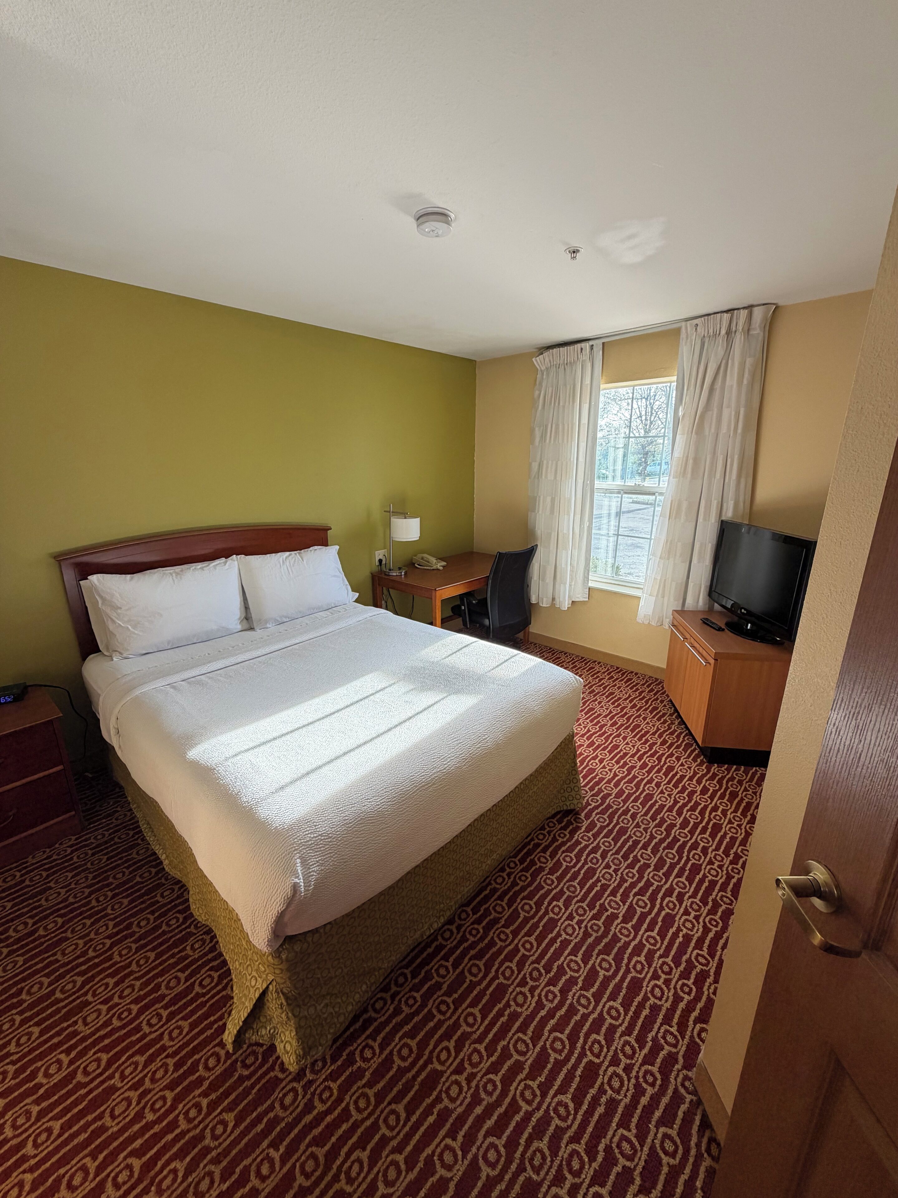 A hotel room with a bed, a desk, a chair, a television, and a window with curtains.