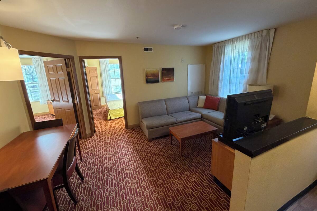 A hotel room with a sofa, a TV, a desk, and a patterned carpet.