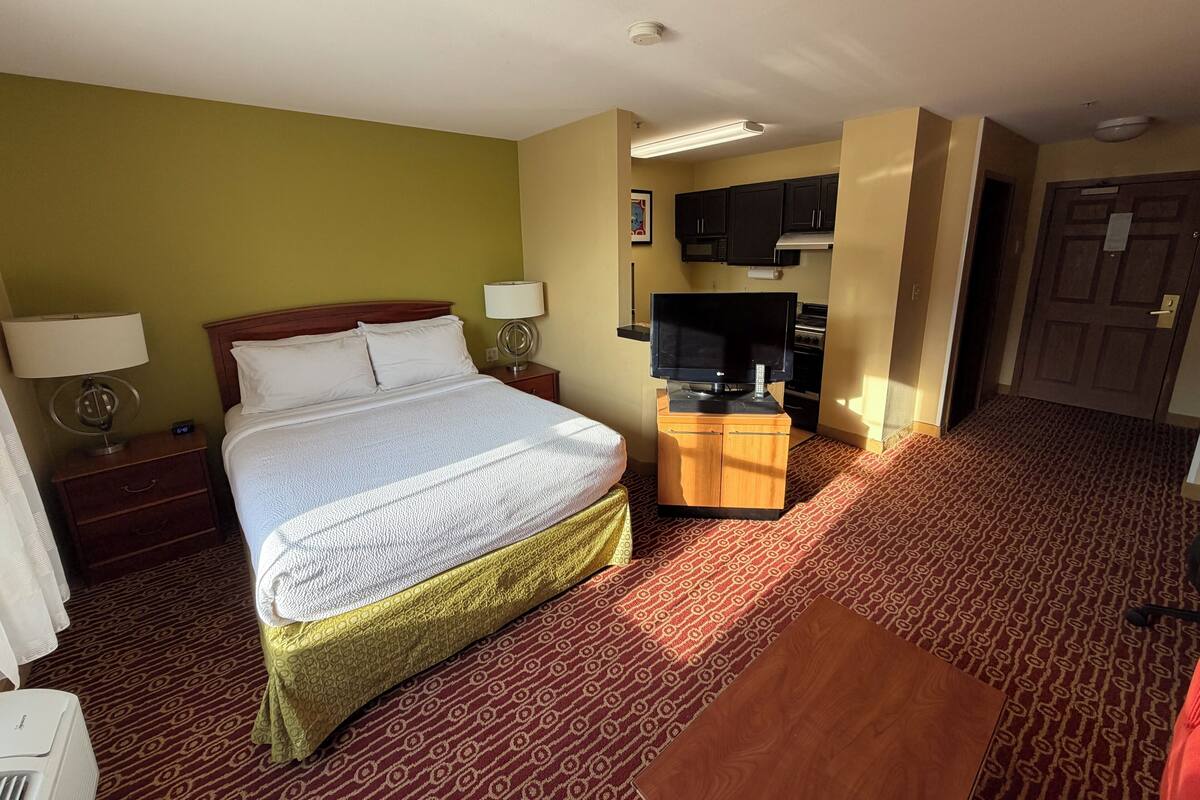 A hotel room with a bed, a desk with a television, a microwave, and a door.