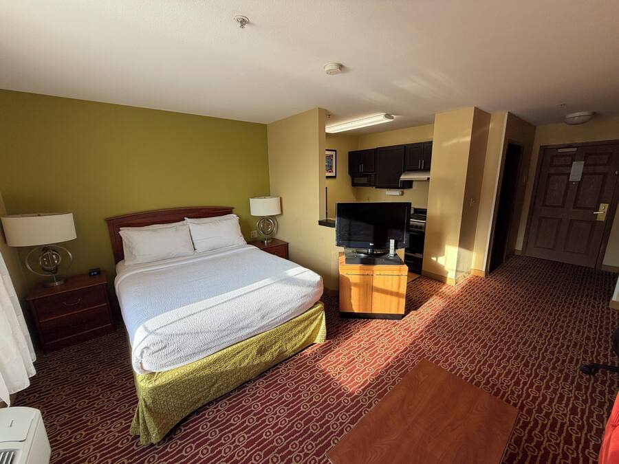 A hotel room with a bed, a desk with a television, a microwave, and a door.