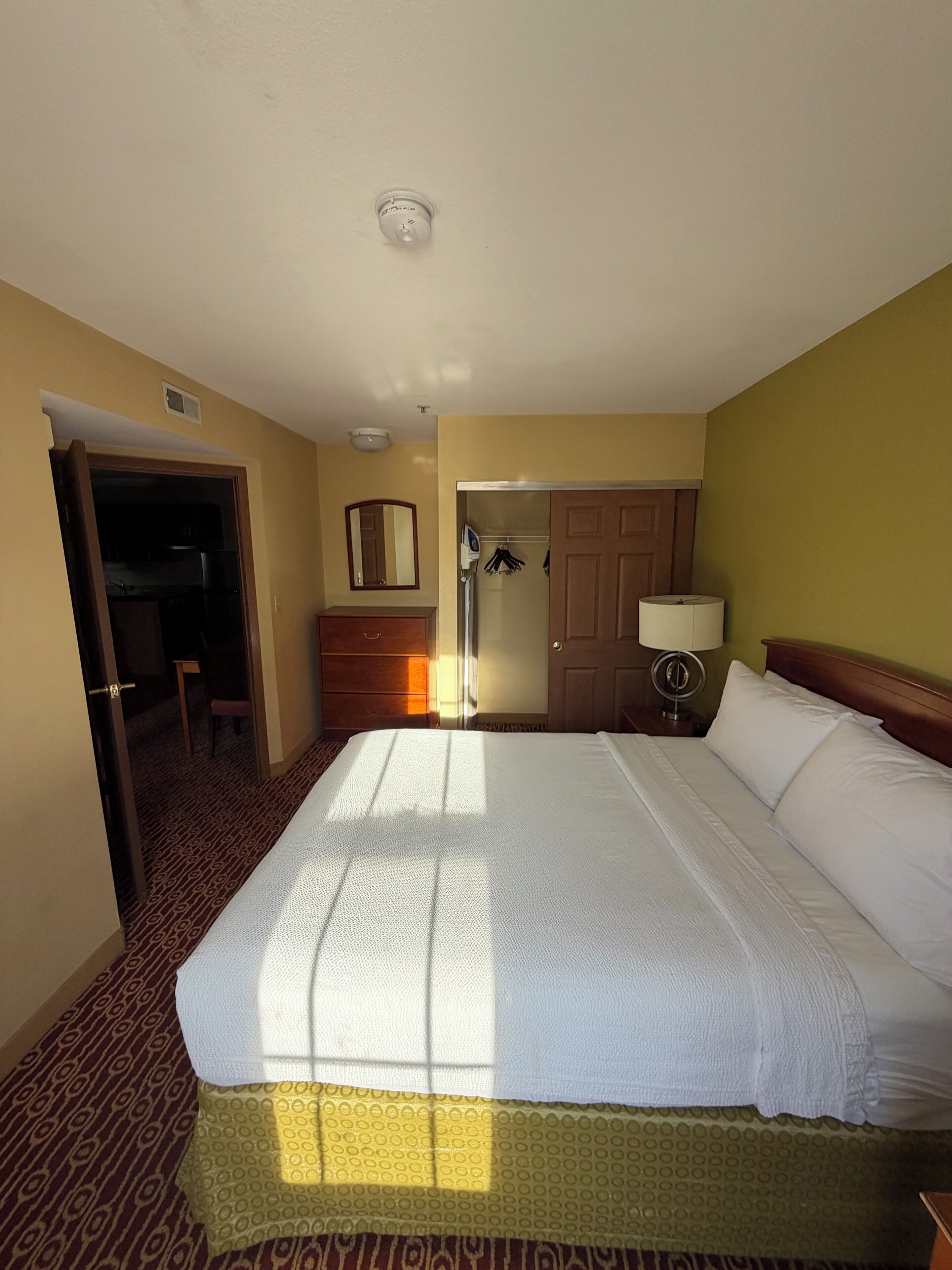 A hotel room with a bed, a door, a mirror, a lamp, and a wardrobe.