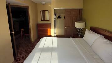 A hotel room with a bed, a door, a mirror, a lamp, and a wardrobe.