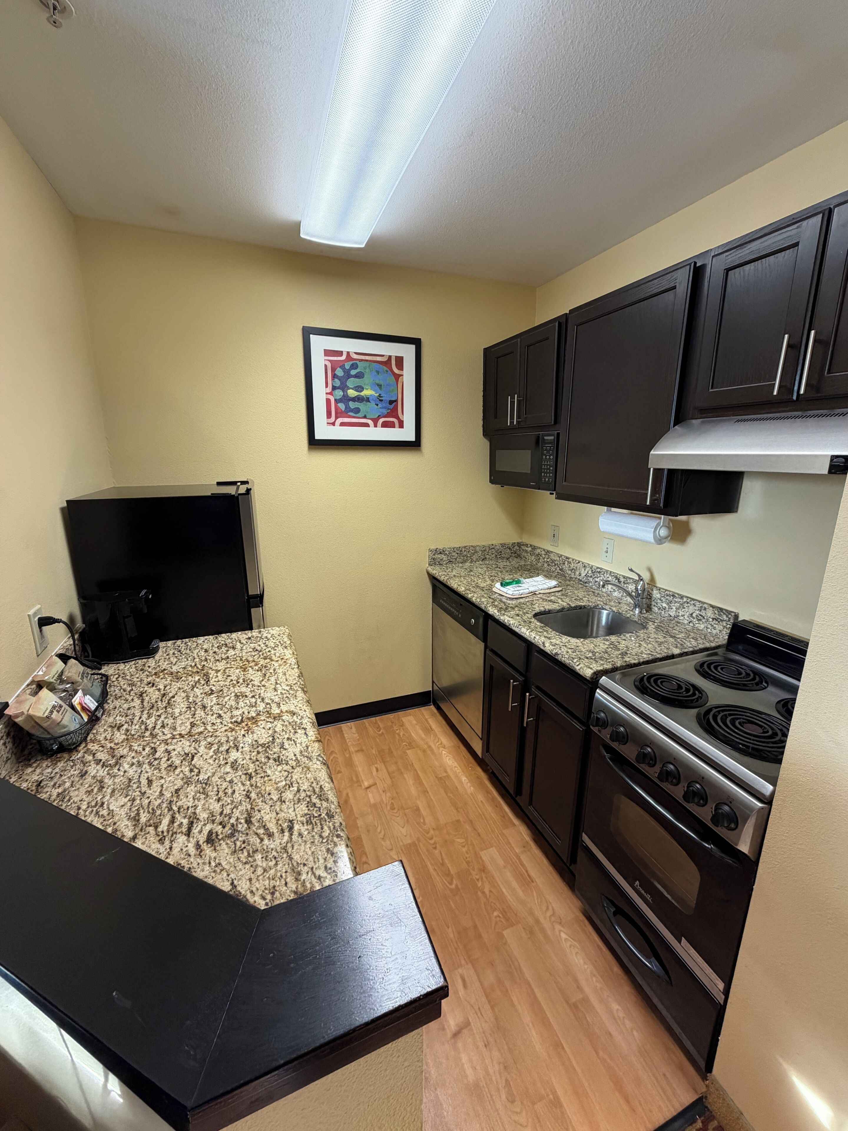 A compact kitchen with a granite countertop, stainless steel appliances, and dark cabinetry.