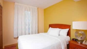 Una habitación de hotel con cama, mesita de noche, lámpara y ventana con cortinas.