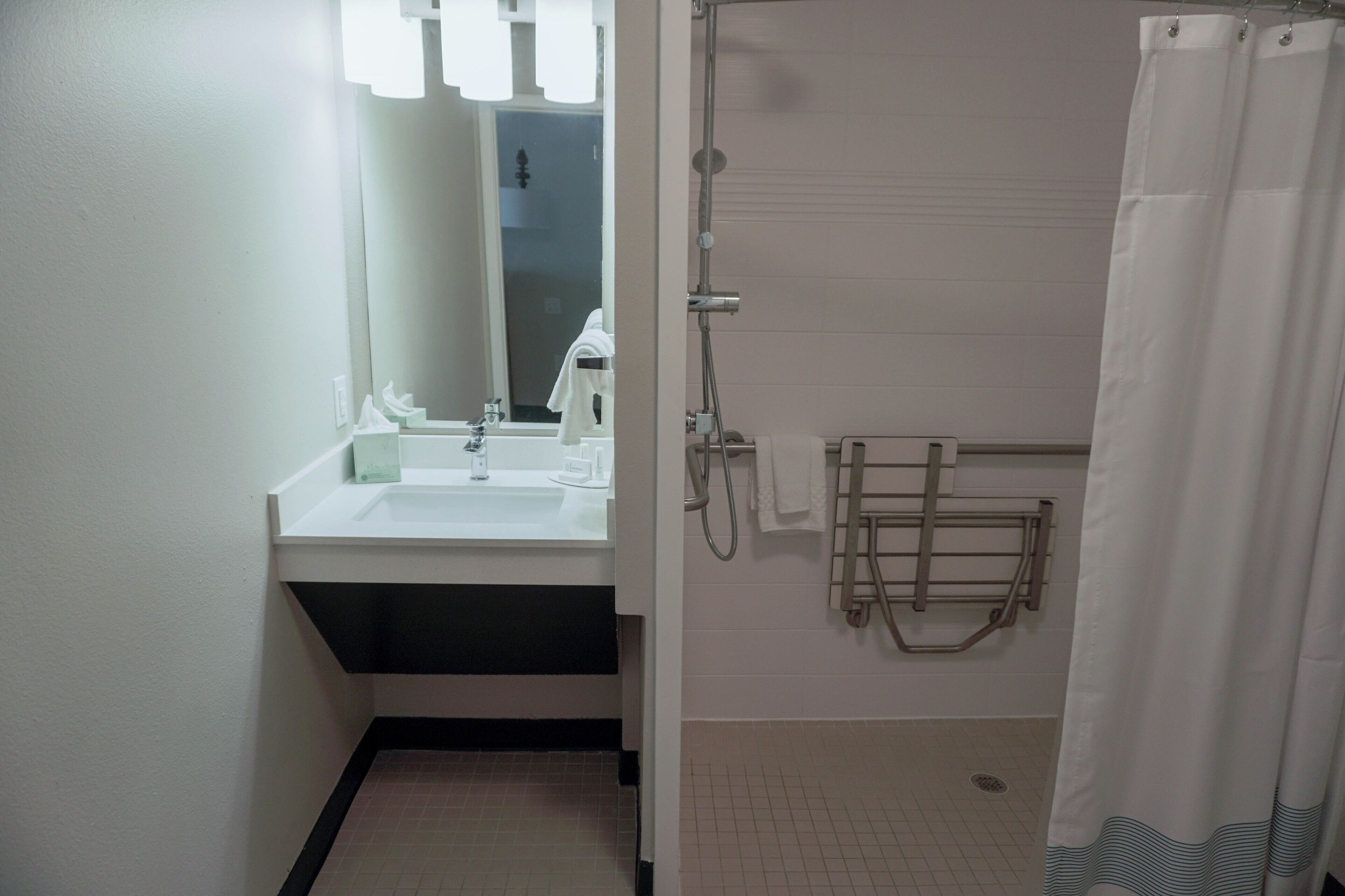 A bathroom with a sink, mirror, shower, and towel rack.