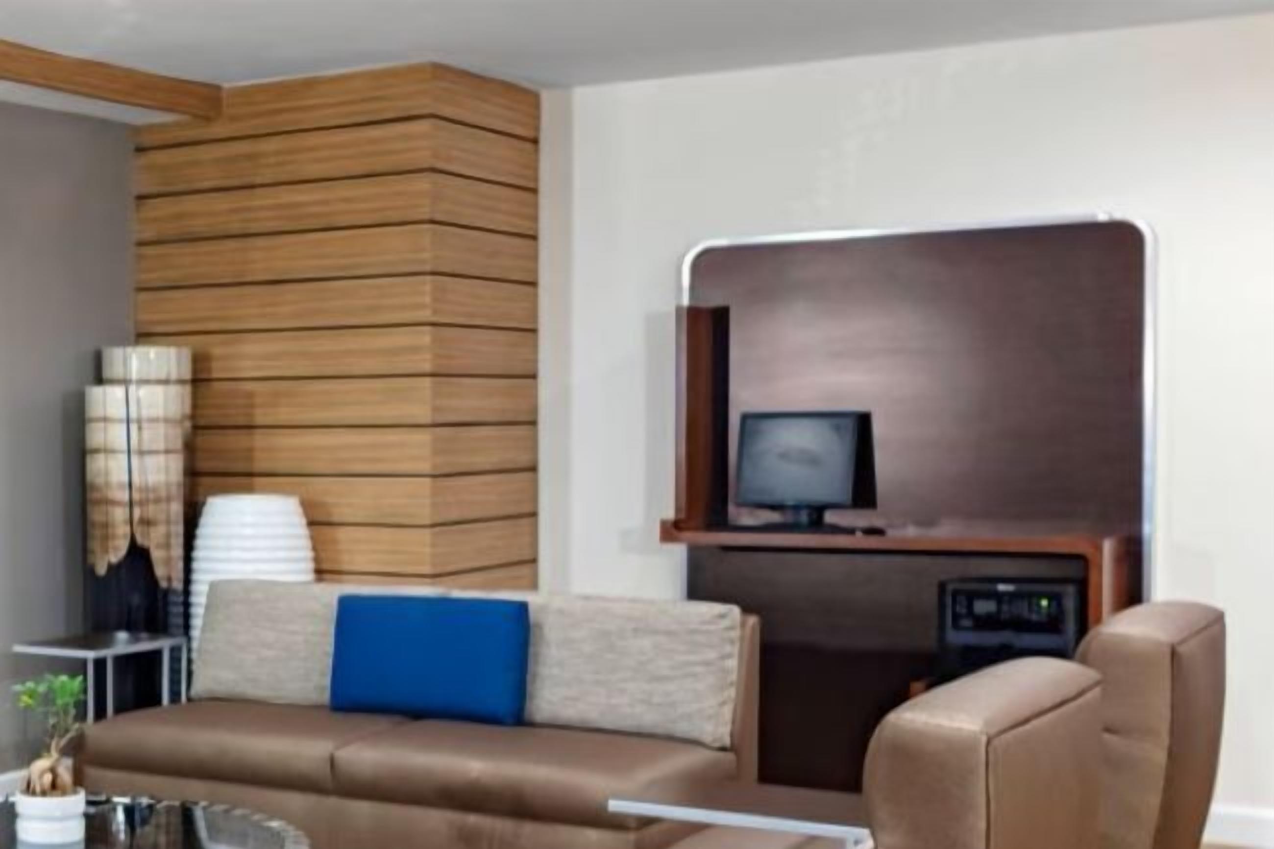 A modern living room with a brown leather sofa, a side table with a lamp, and a television mounted on a wooden wall.