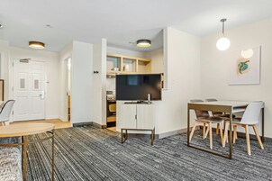 Una habitación de hotel moderna con zona de comedor, televisor de pantalla plana y cocina.