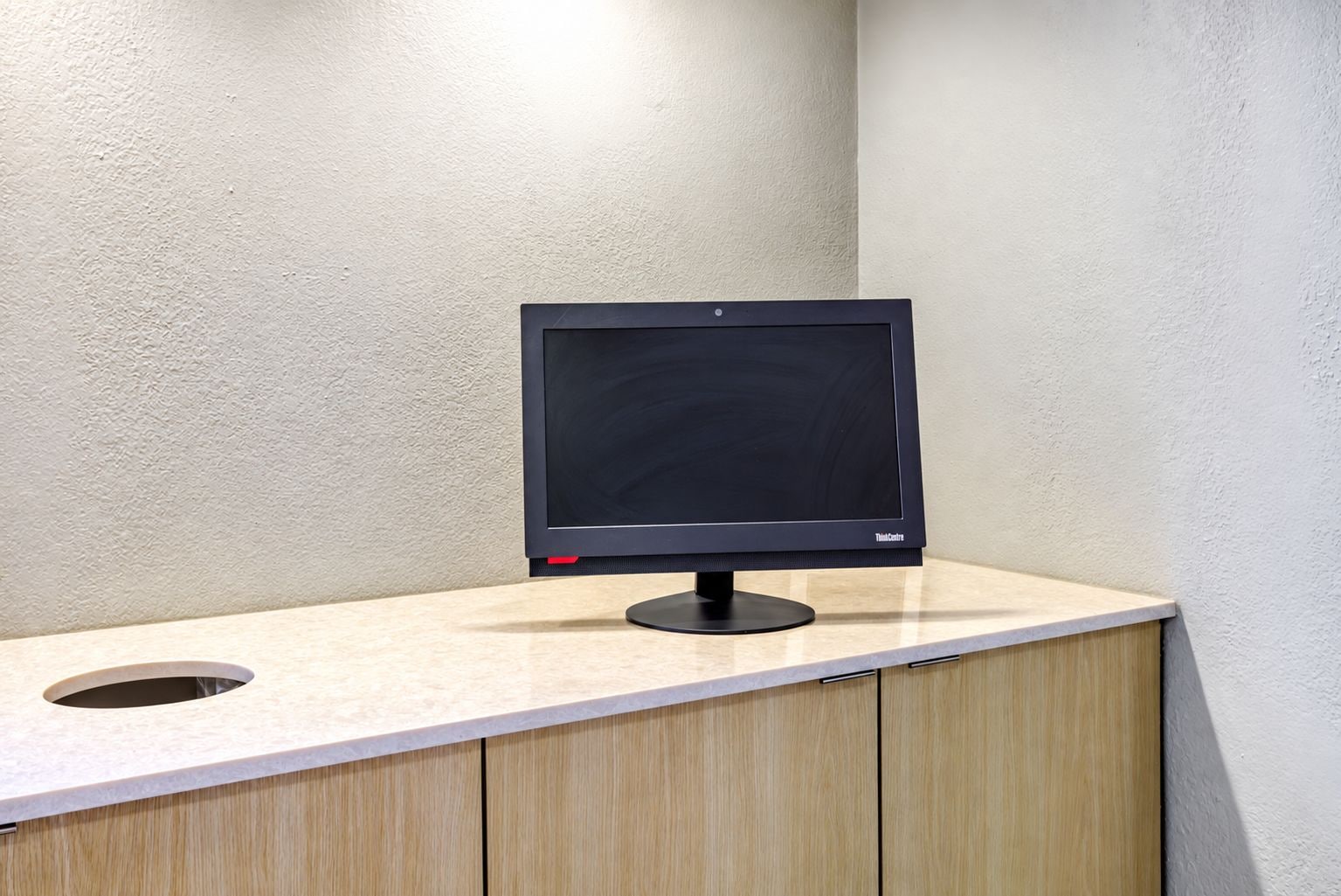A flat-screen monitor on a light-colored countertop with a hole cutout, against a textured wall.