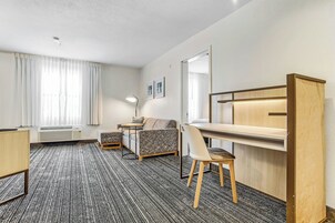 Habitación de hotel con cama, escritorio, silla, sofá, lámpara y ventana con cortinas.