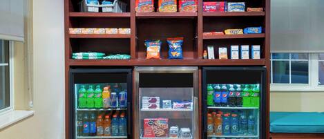 A vending machine with snacks and drinks, a refrigerator with beverages, and a window with a view.