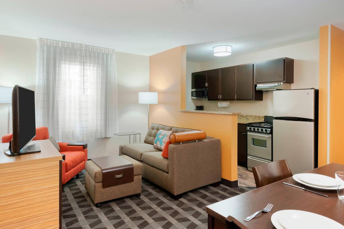Een compacte hotelkamer met een kitchenette, een bank, een eettafel en een televisie.
