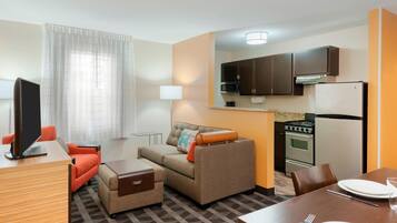 A compact hotel room with a kitchenette, a sofa, a dining table, and a TV.