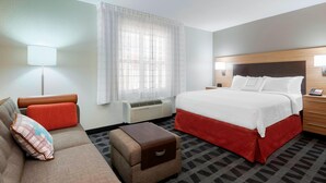 A hotel room with a bed, a sofa, a small table, a lamp, and a window with curtains. - TownePlace Suites by Marriott Savannah Midtown (Savannah)