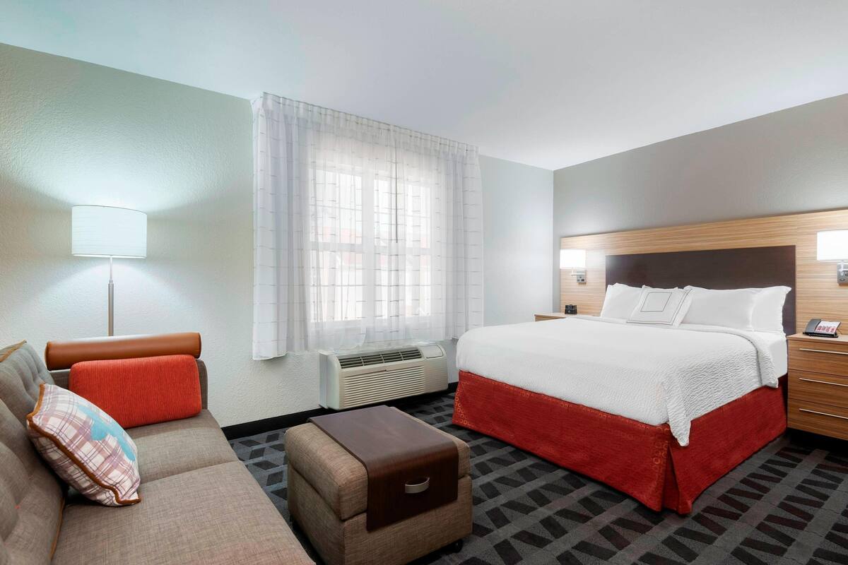 Hotelkamer met een bed, een bank, een tafeltje, een lamp en een raam met gordijnen.