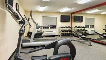 A gym with cardio machines, dumbbells, and a TV.