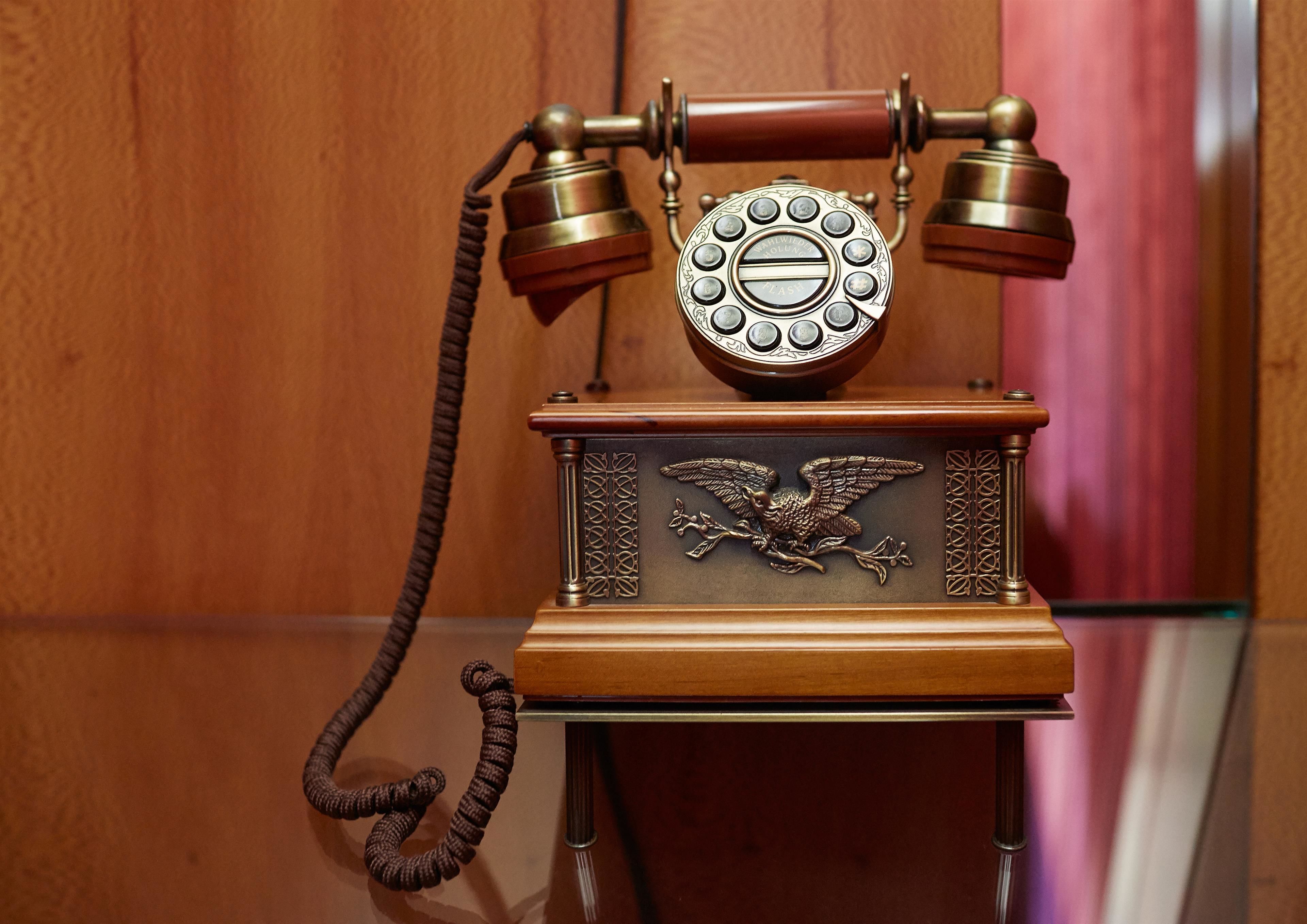 A vintage rotary dial telephone with an eagle emblem on the base, mounted on a wooden stand.