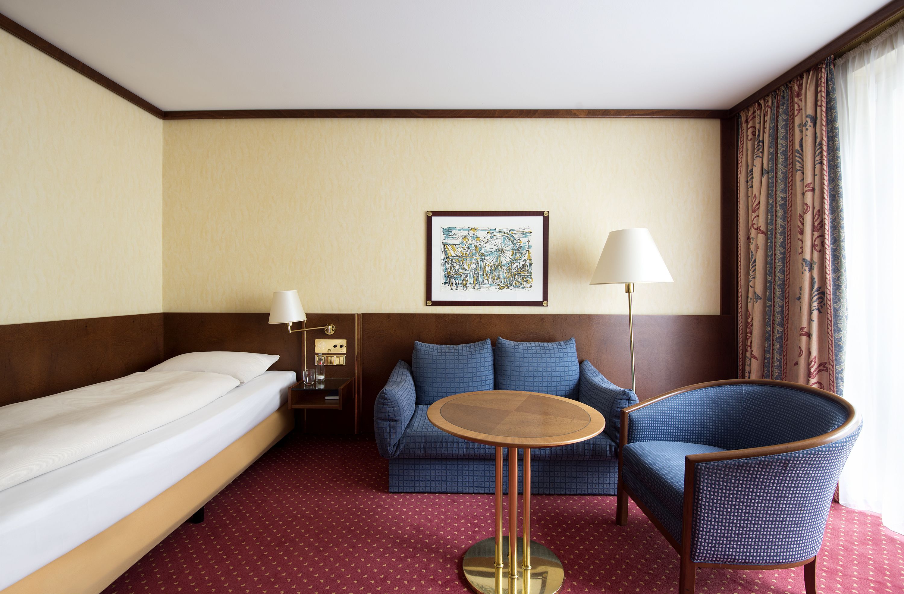 Una habitación de hotel con una cama, un sofá azul, una mesa redonda y una lámpara.