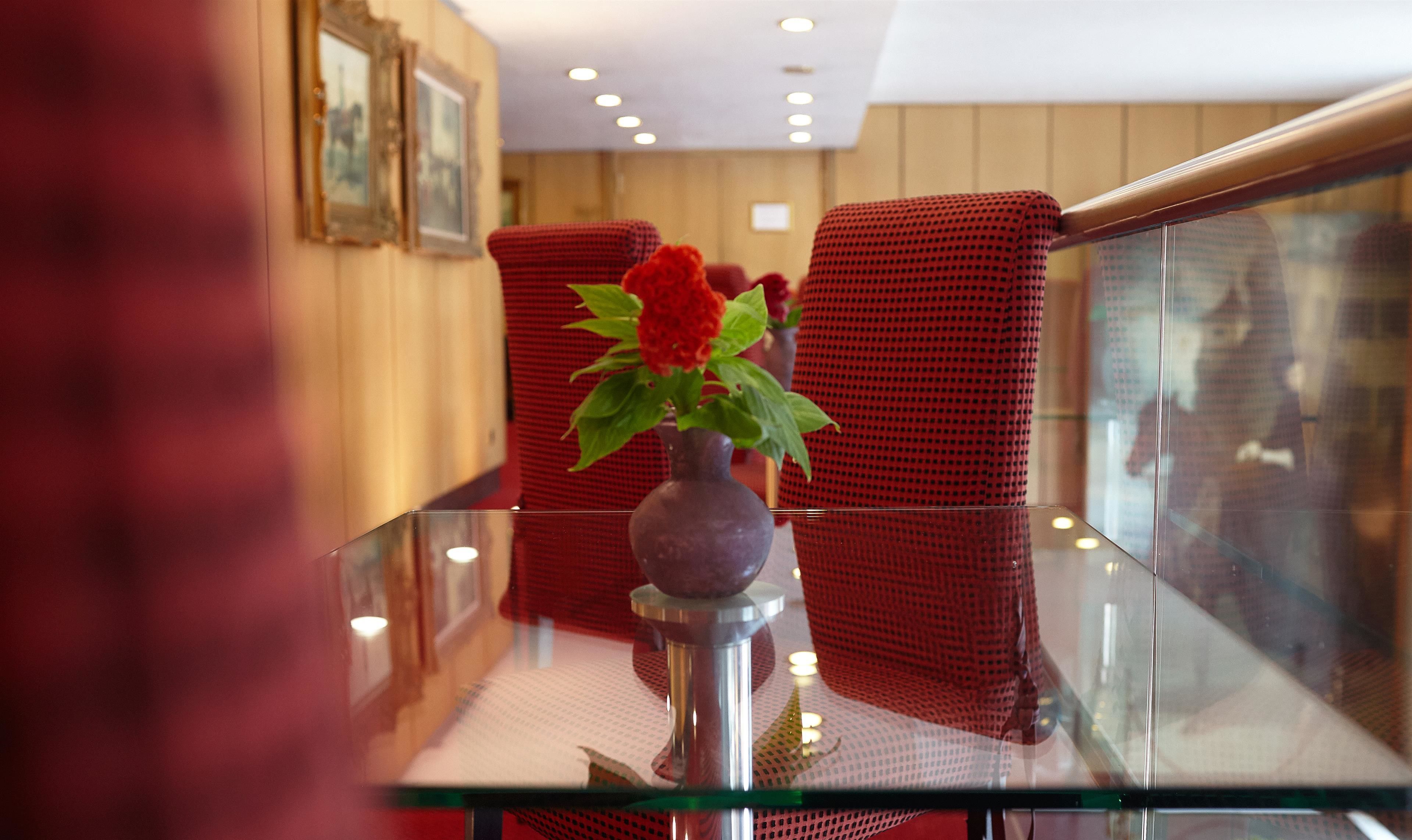 A glass table with a vase of flowers, red upholstered chairs, and framed pictures on the wall.