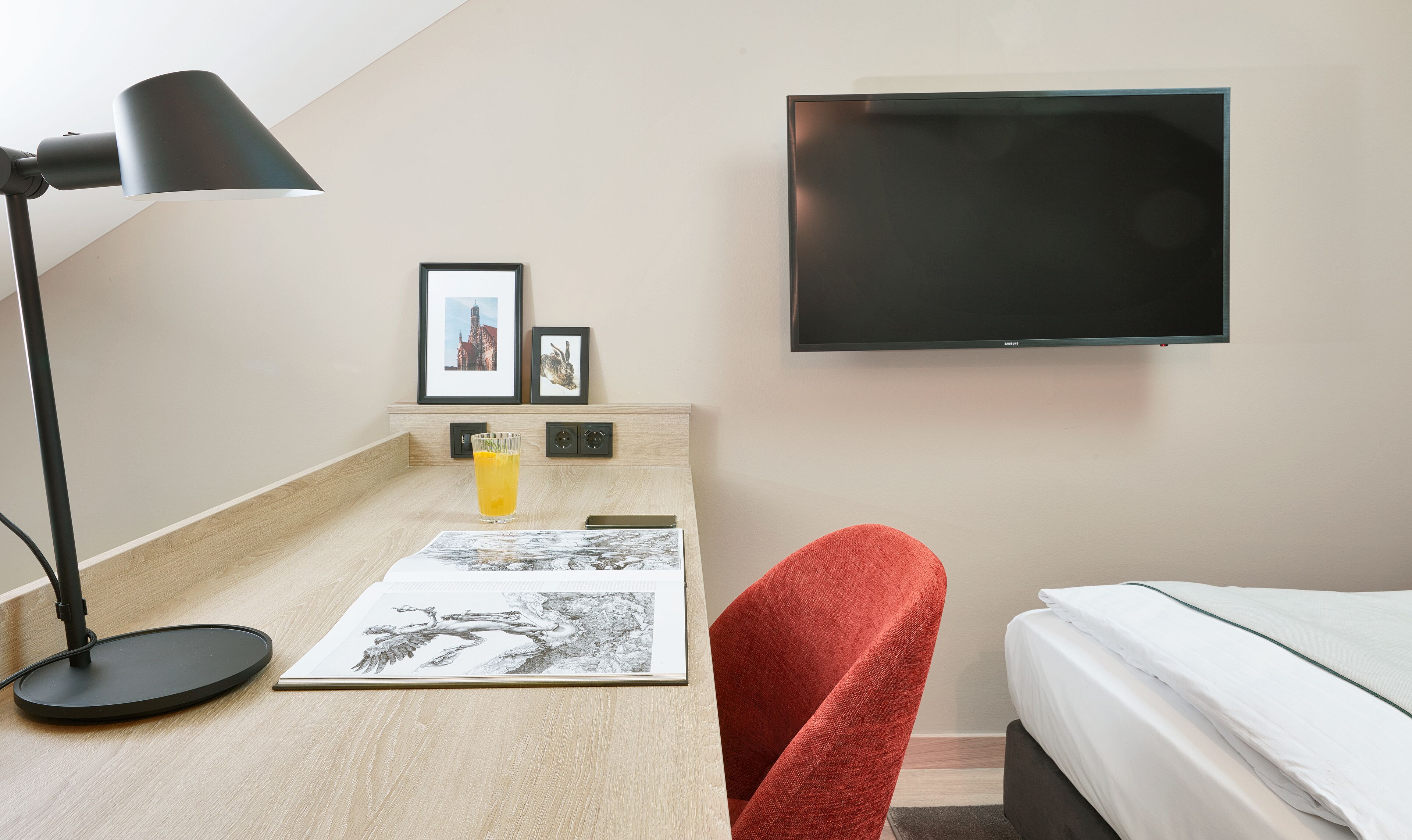 Une chambre d’hôtel avec un lit, un bureau doté d’une lampe, une télévision et des œuvres d’art accrochées au mur.