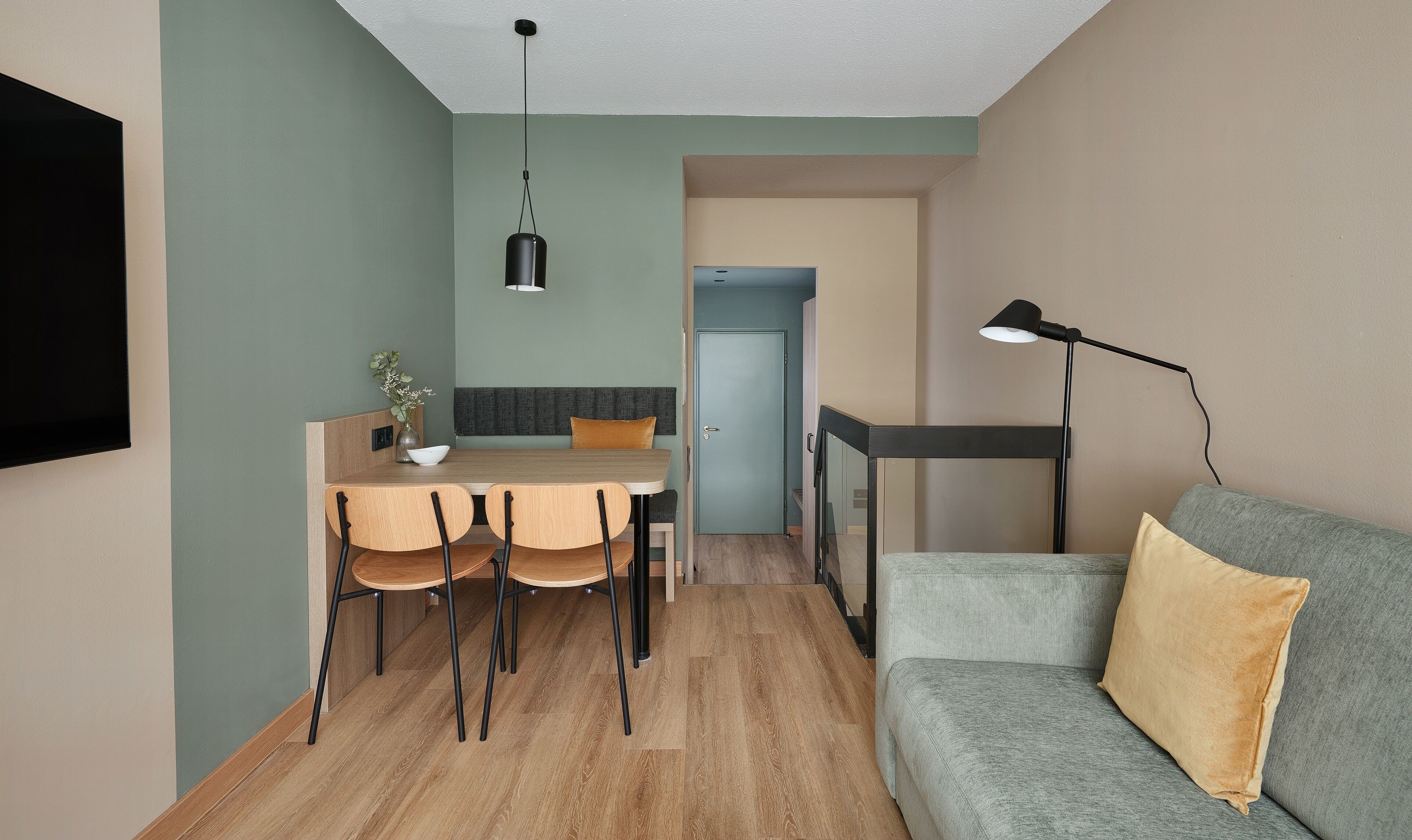 Un espace de vie compact comprenant un coin repas, un canapé et un téléviseur fixé au mur.