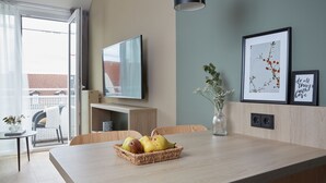 A modern dining area with a wooden table, a basket of pears, a vase with flowers, and a flat-screen TV mounted on the wall. - Living Hotel Nürnberg (Nuremberg)