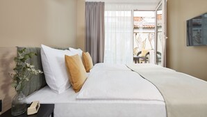 A hotel room with a bed, a nightstand, a vase with flowers, and a view of the outside. - Living Hotel Nürnberg (Nuremberg)