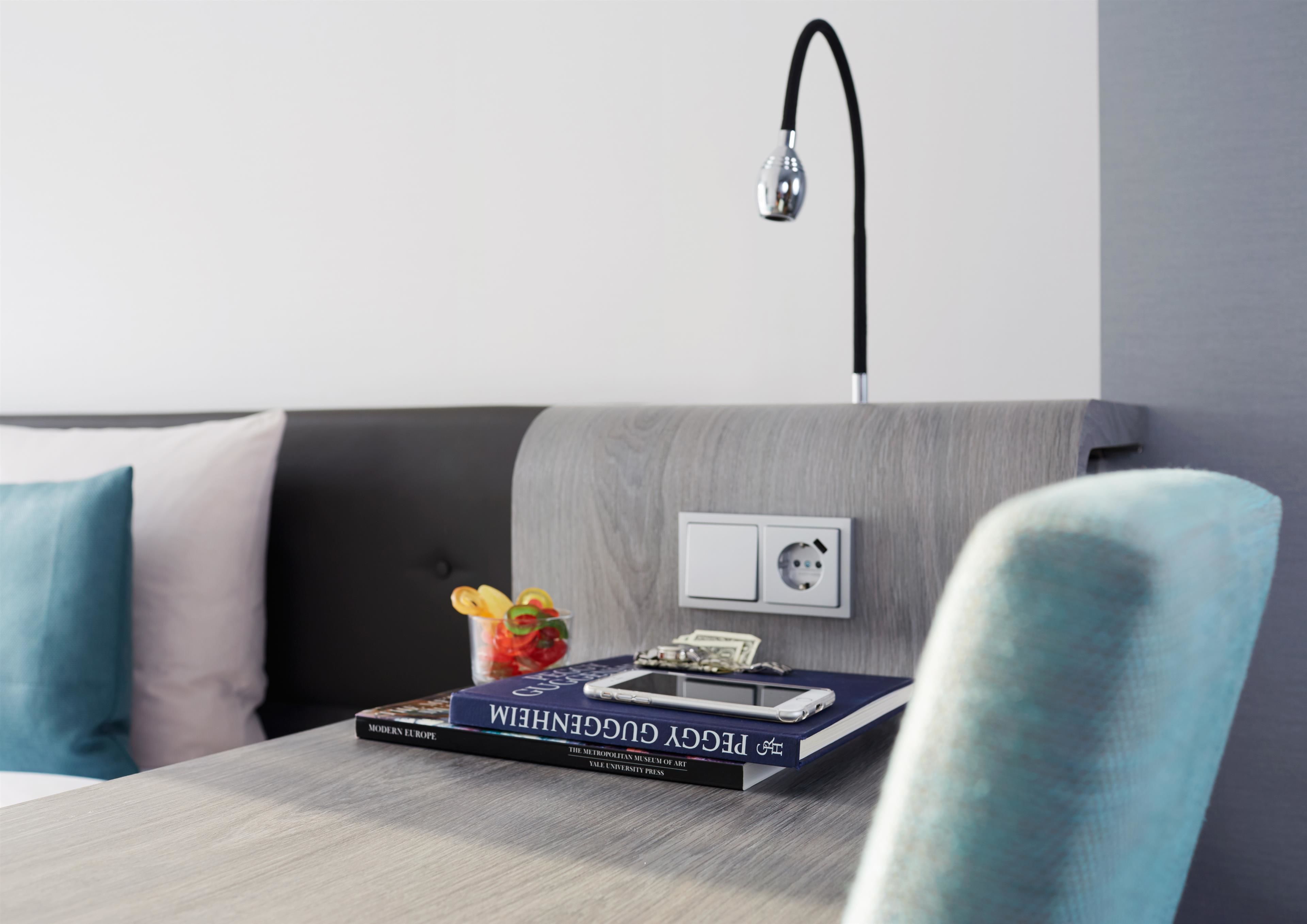 A modern room with a grey sofa, a table with books and a smartphone, and a wall socket.