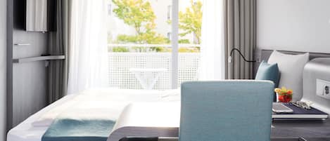Une chambre d’hôtel avec un lit, un bureau et une chaise, une télévision et une vue sur l’extérieur.