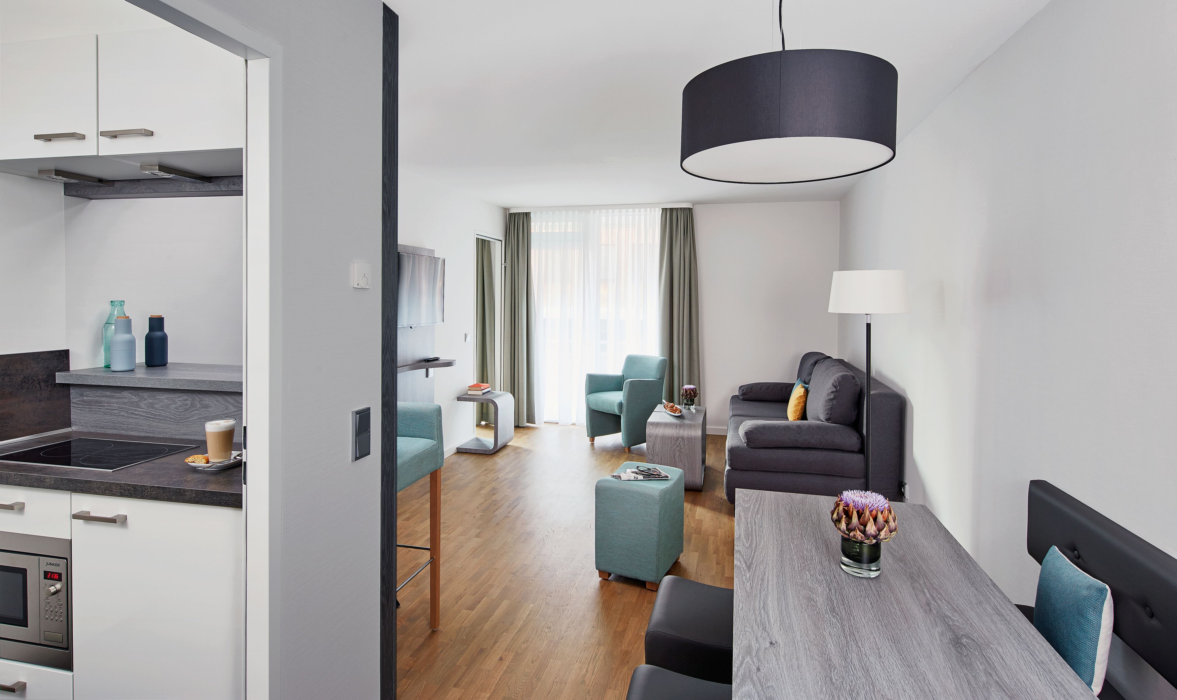 A modern, well-lit living area with a dining table, sofa, and a kitchen area with a microwave.