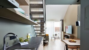 A modern kitchen with a built-in sink, a staircase, a dining area with a table and chairs, and a TV mounted on the wall. - Living Hotel Nürnberg (Nuremberg)