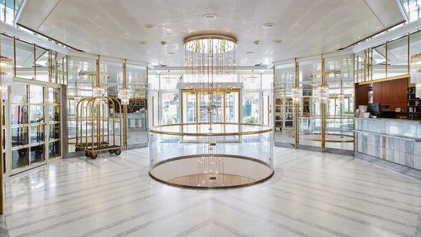Um hall amplo com uma plataforma circular central, guarda-corpos de vidro e um balcão de recepção.