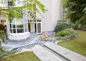 A modern building with a glass entrance, outdoor seating area, and a well-maintained garden. - Living Hotel Kaiser Franz Joseph (Vienna)