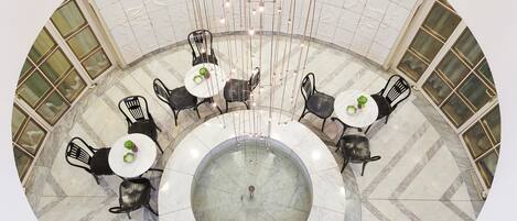 A circular dining area with marble flooring and black chairs around white tables, featuring a central fountain.