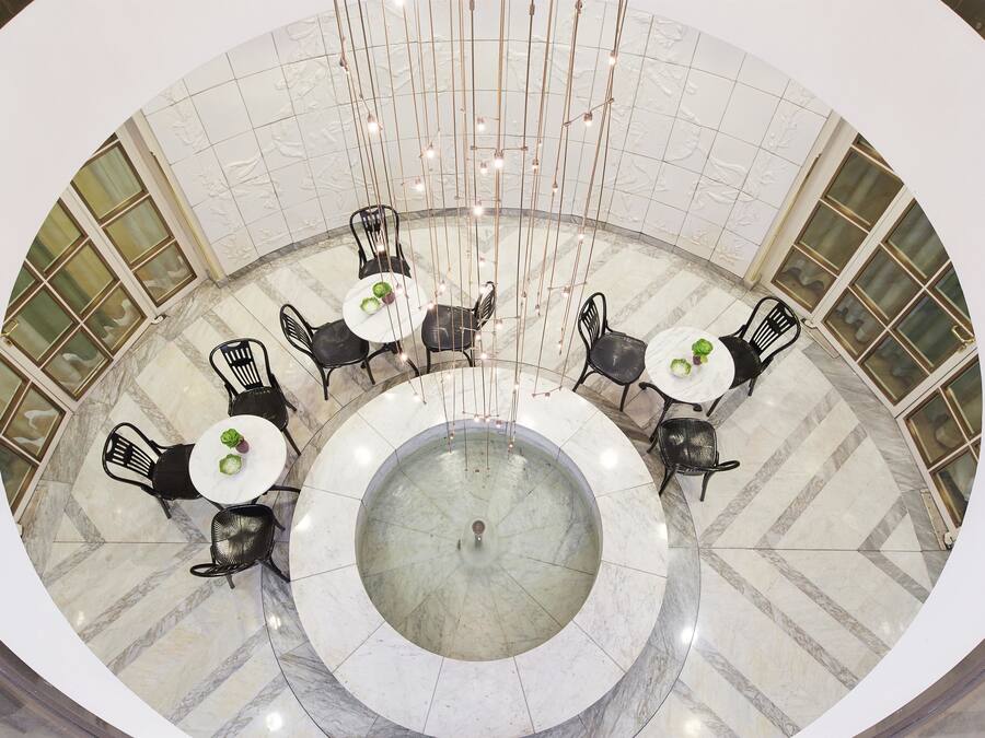 Un comedor circular con suelo de mármol y sillas negras alrededor de mesas blancas, que incluye una fuente central.