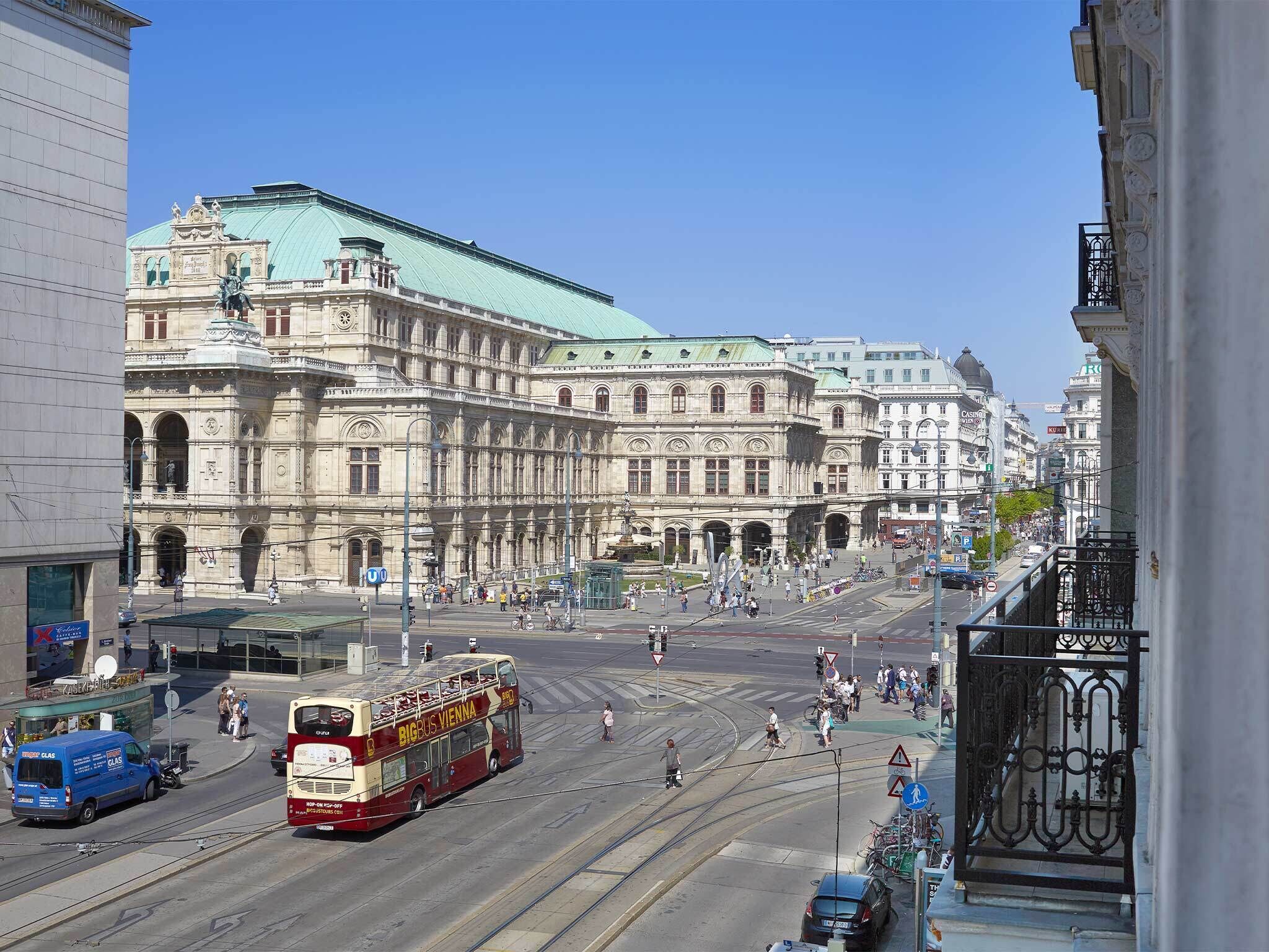 A double-decker bus on a city street with historic buildings in the background.