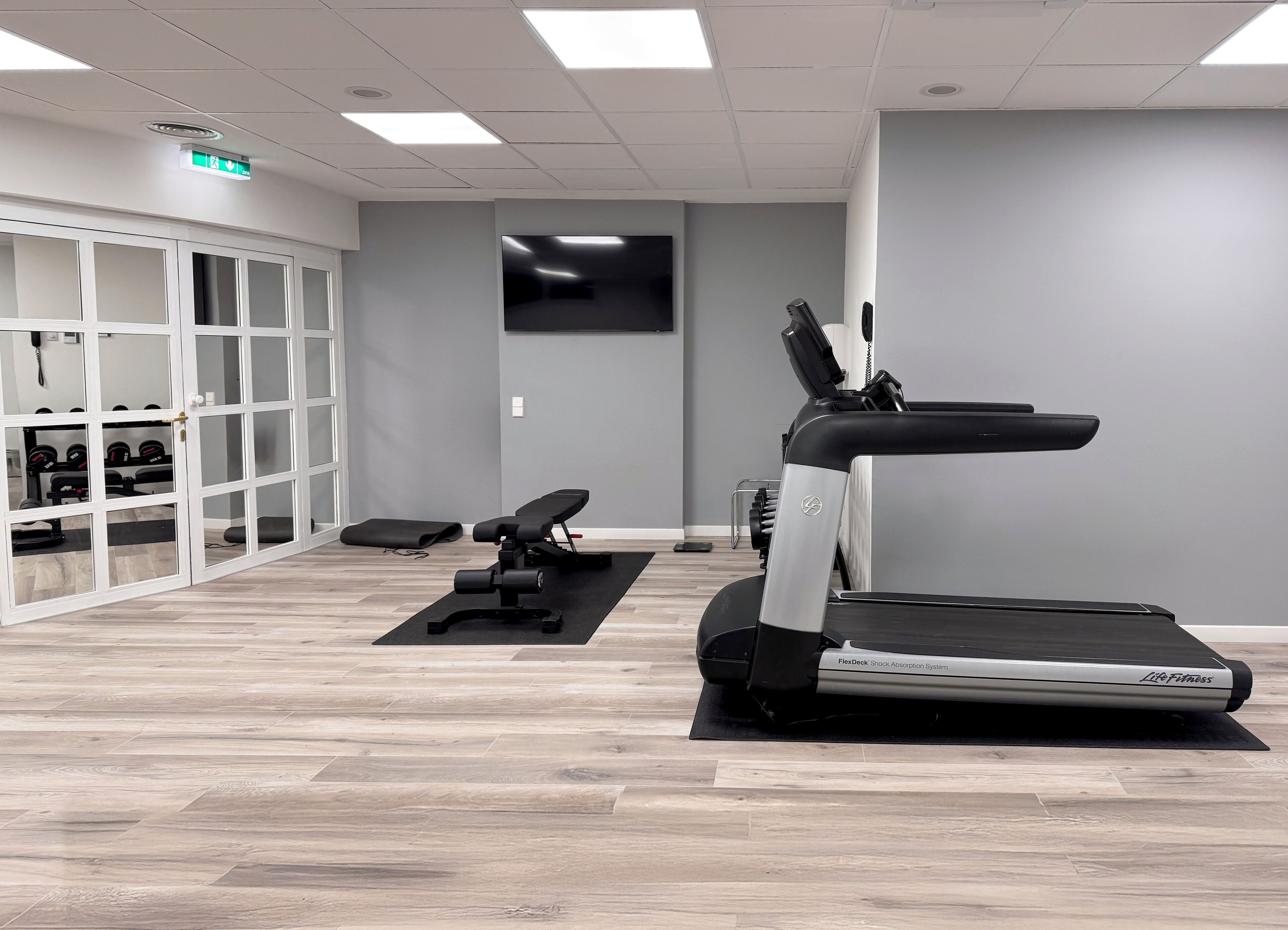 Et fitnessrum med løbebånd, vægtbænk og håndvægte.