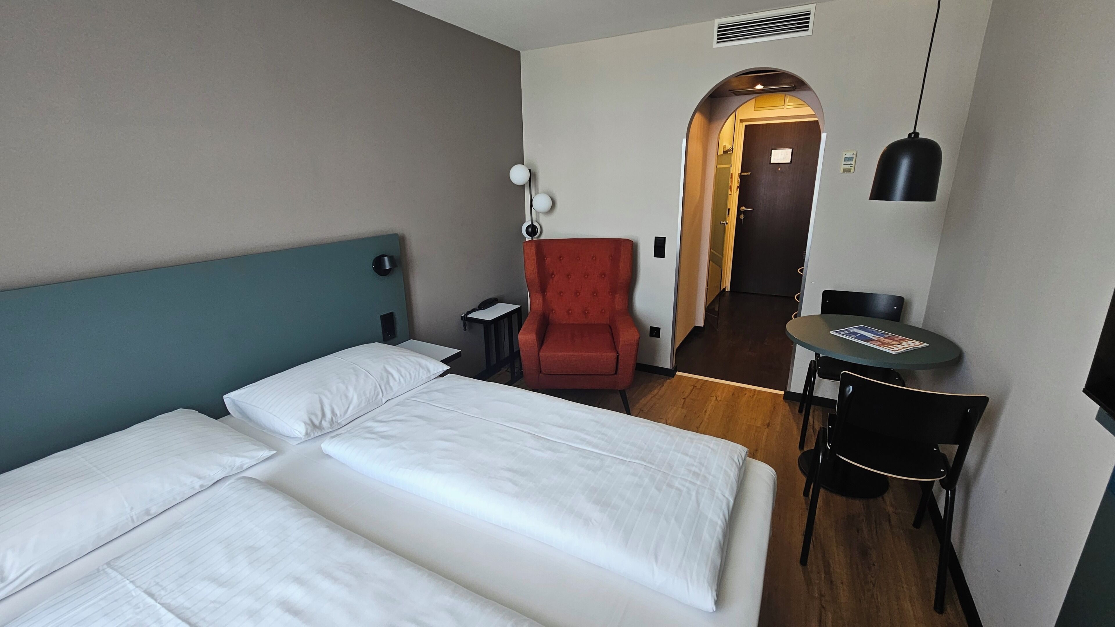 Une chambre d’hôtel avec un lit, un fauteuil rouge, une petite table et un bureau avec une chaise.