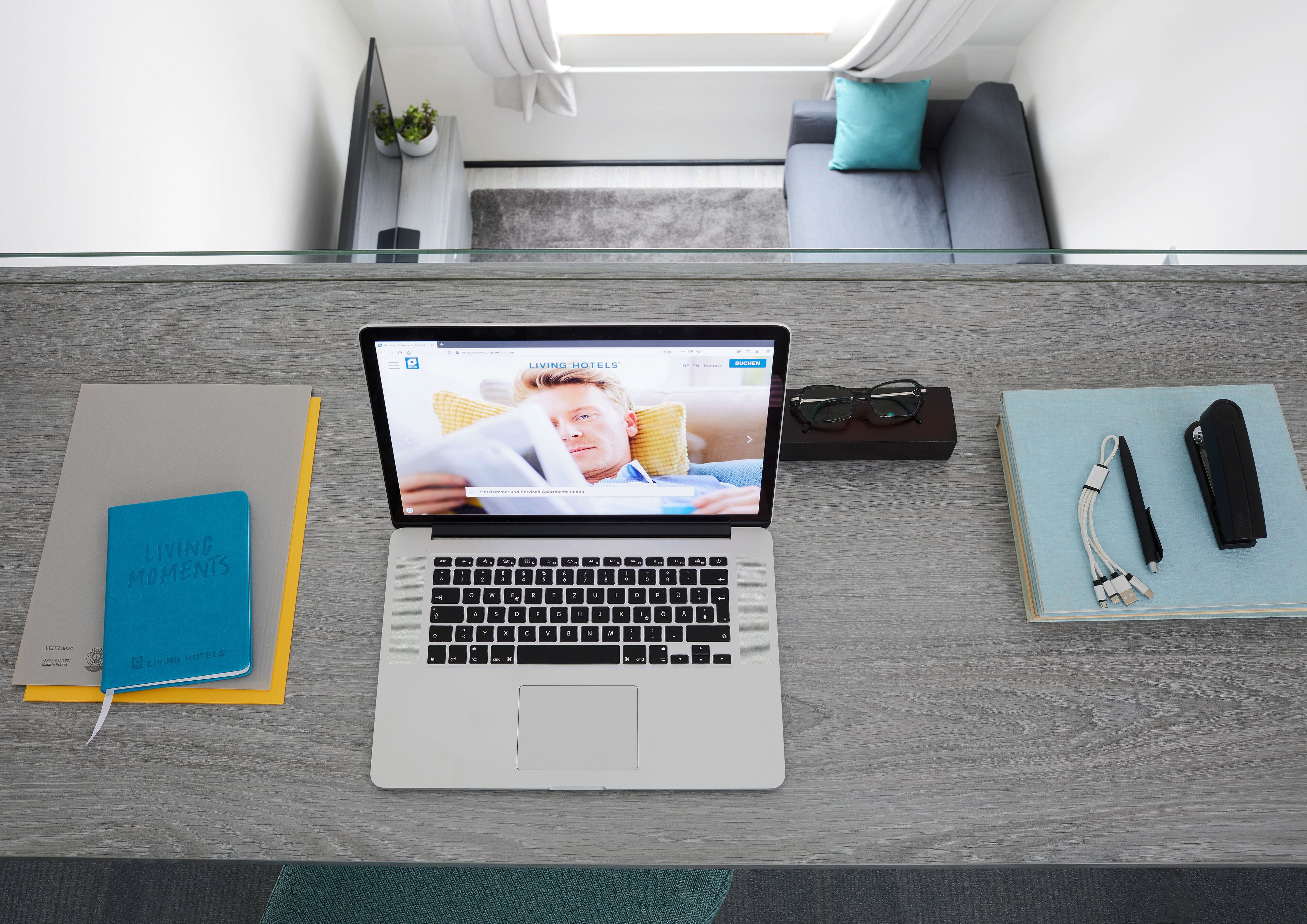 A laptop on a desk with a notebook, pen, and glasses beside it.