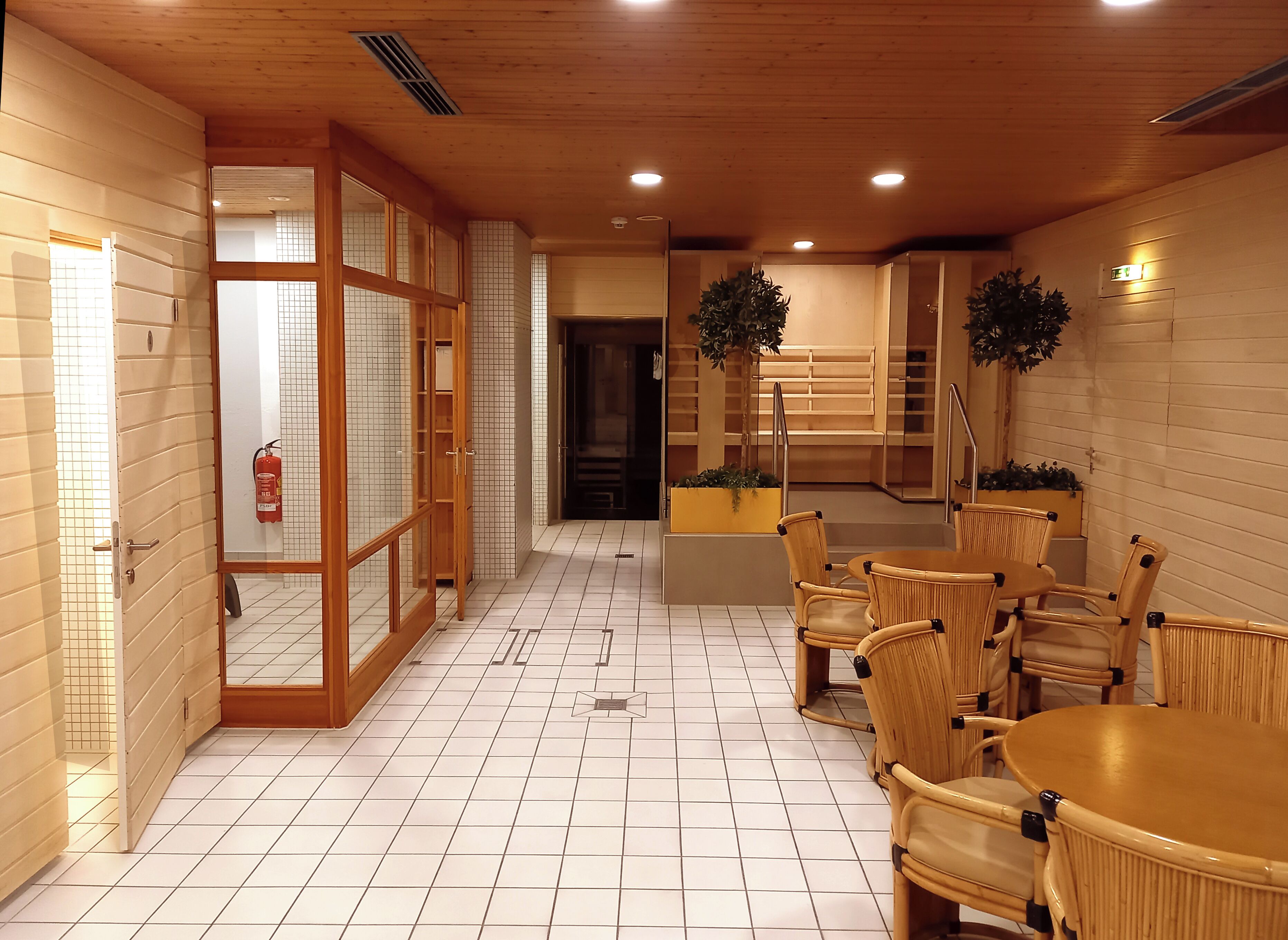 A hotel lobby with a tiled floor, wooden walls, a reception desk, and wicker furniture.
