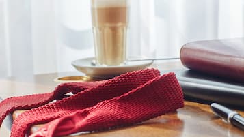 A close-up of a red knitted item on a wooden surface with a pen and a glass of a beverage in the background.