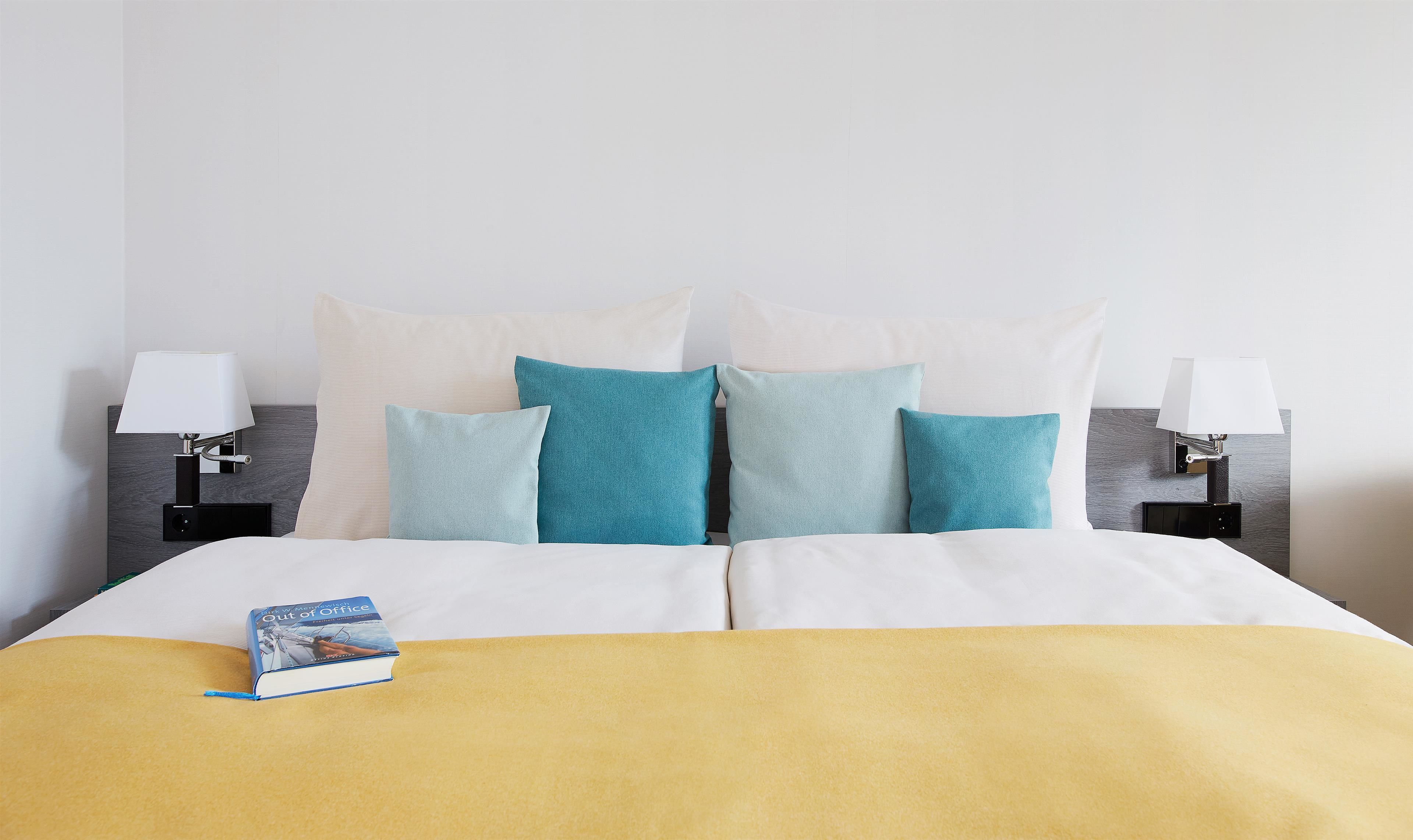 A neatly made bed with a yellow blanket, a book, and multiple pillows in shades of blue and white.