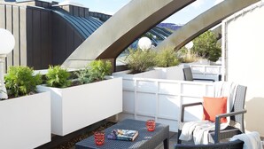 Terraço no telhado com vasos brancos, uma mesa com um livro e um copo, e uma cadeira com almofada.